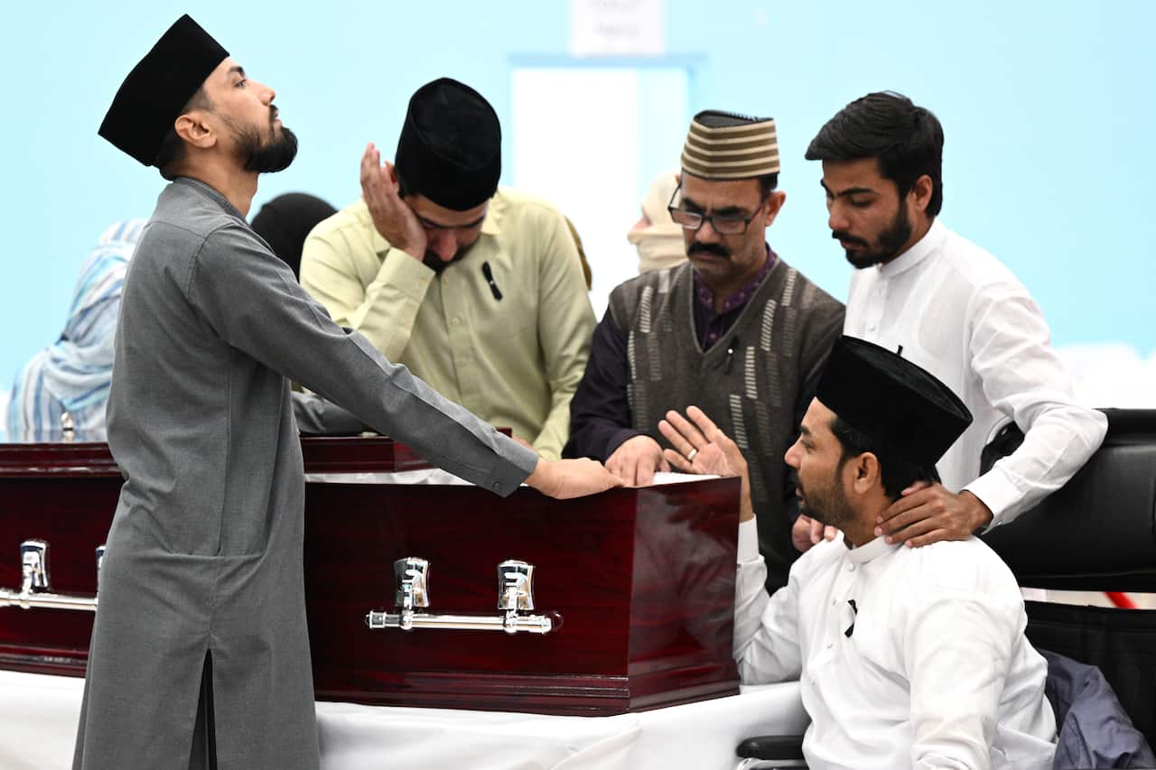 A person in a wheel chair speaks to other mourners by the casket at a funeral.