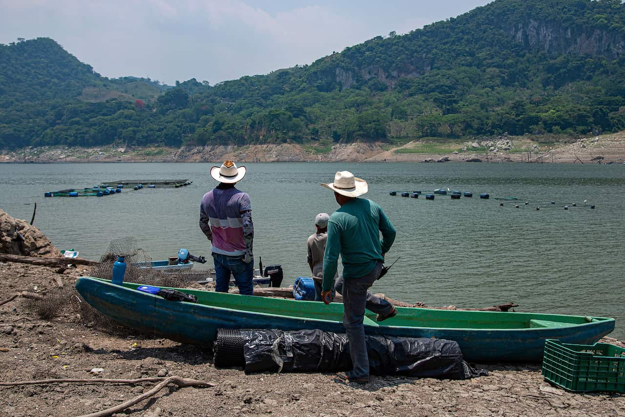 Men in cowboy hats stand next to a canoe and survey a low river