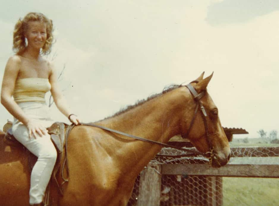 An old photo of a young woman mounted on a horse. She is smiling.