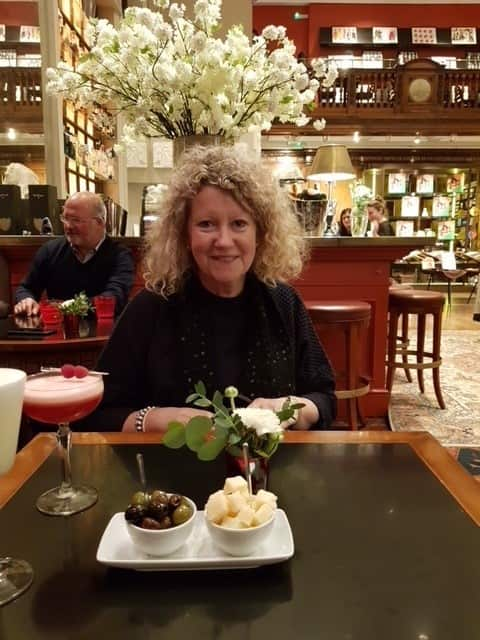 A woman sits in a bar with a cocktail and smiles.