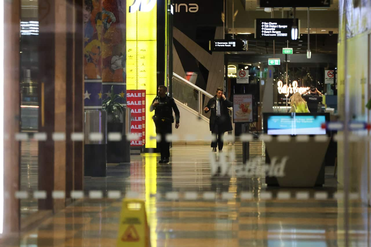 A shopper talking on the phone walks behind a man in a police uniform.