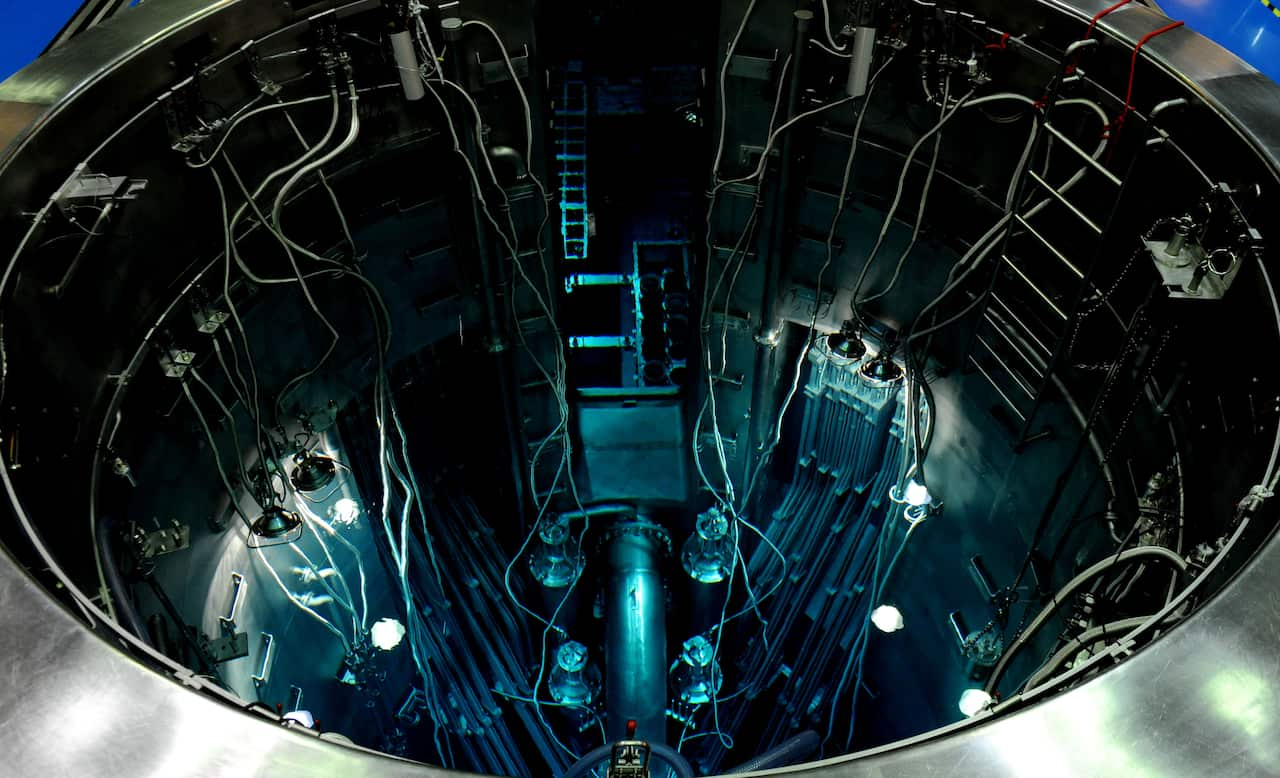 Blue light fills a nuclear reactor, filled with silver tubes and cabling.