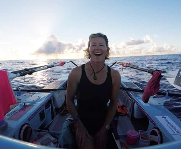 A woman smiling inside a boat. The ocean is visible in the background, and a cloudy sky above.