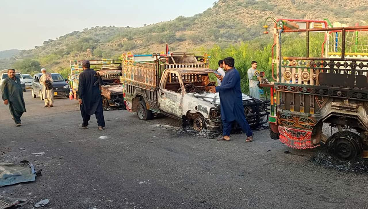 Burnt-out cars with deflated tyres are lined up along the roadside, with men passing by.