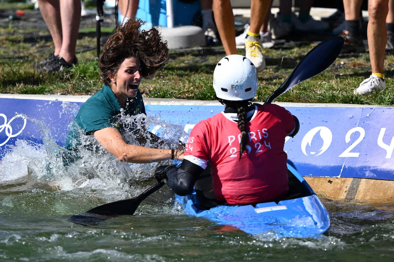 A woman in a green shirt jumps into water next to a woman in a kayak