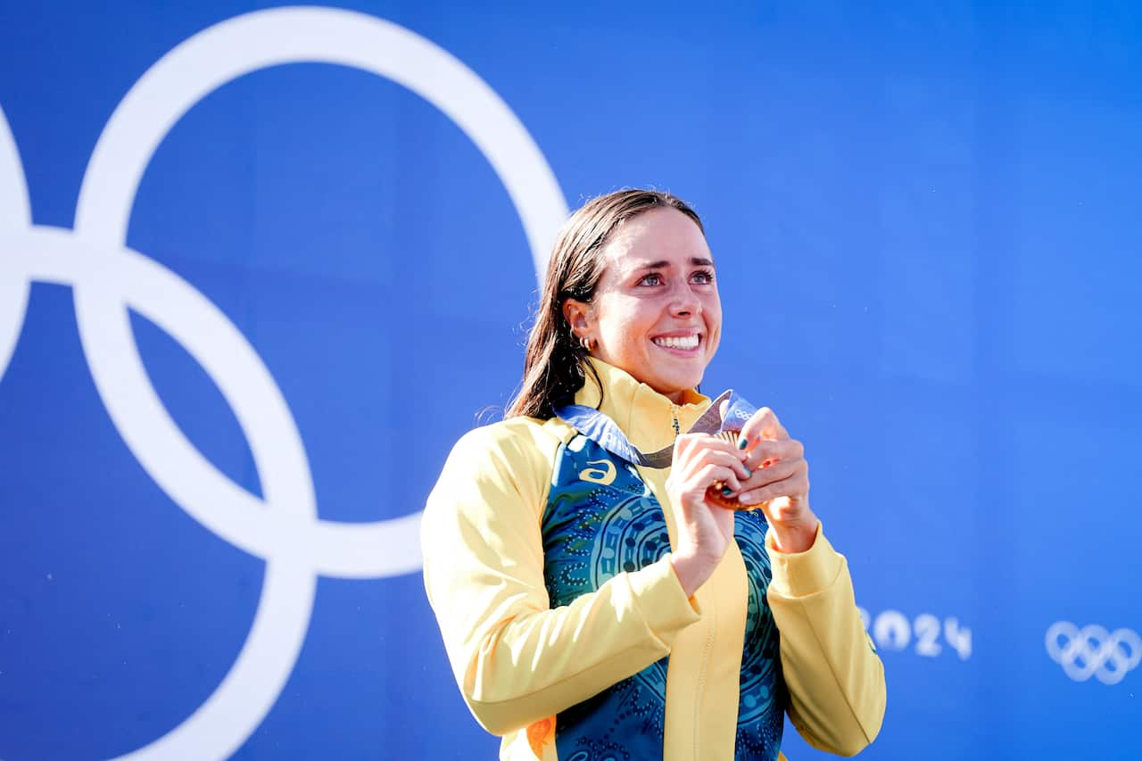 A woman in a yellow and green jacket holds a gold medal