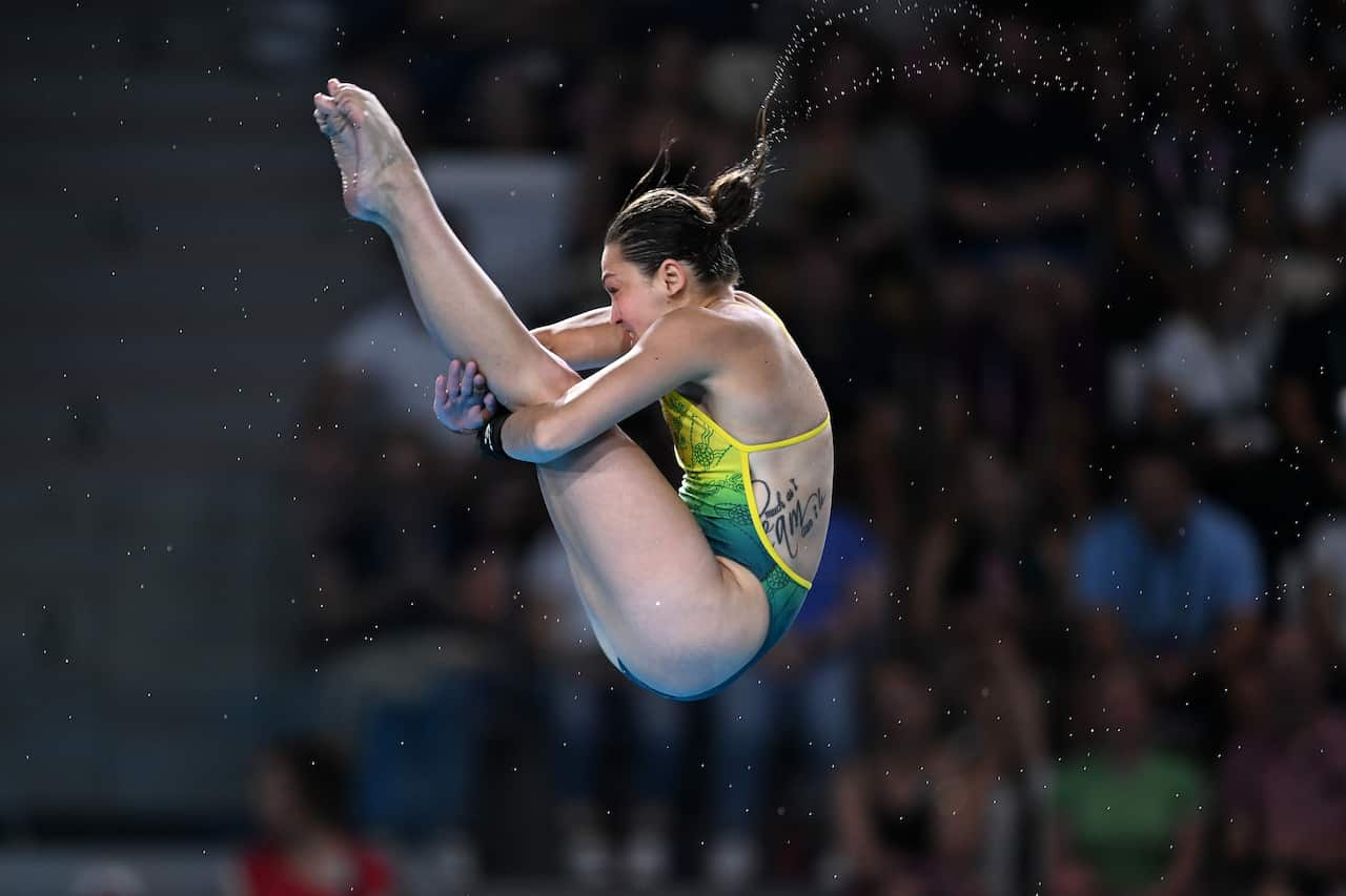 A woman in a yellow and green swmsuit with her legs tucked in a pike