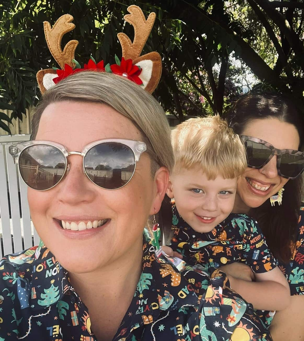 Two adults and a young boy wearing Christmas outfits smiling in a selfie.