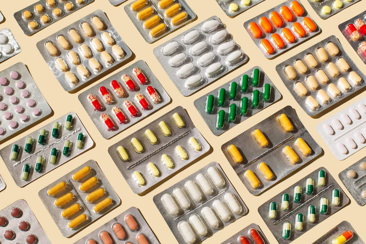 Blisters with colourful pills and capsules on beige background.