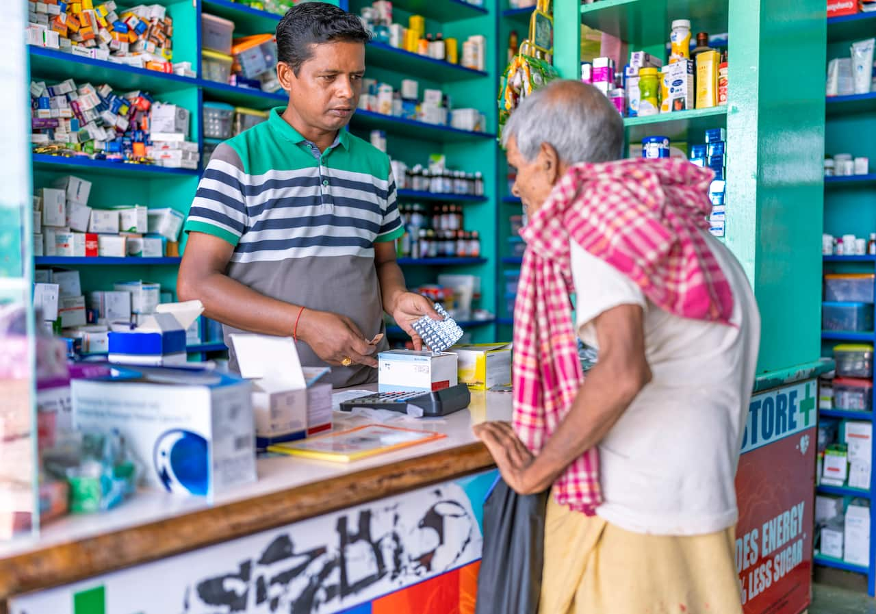 An Indian pharmacist in a pharmacy gives a drug to an elderly man.