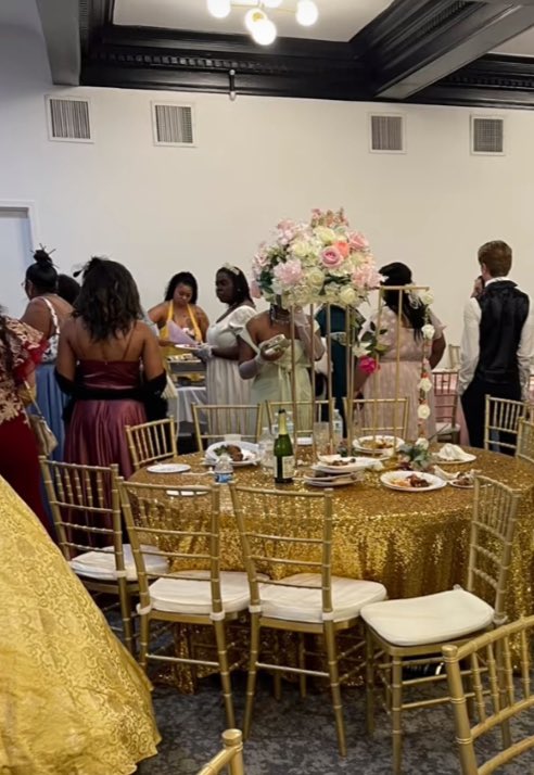 A gold-accented banquet table stands out in a festive gathering, with guests mingling around in formal attire.