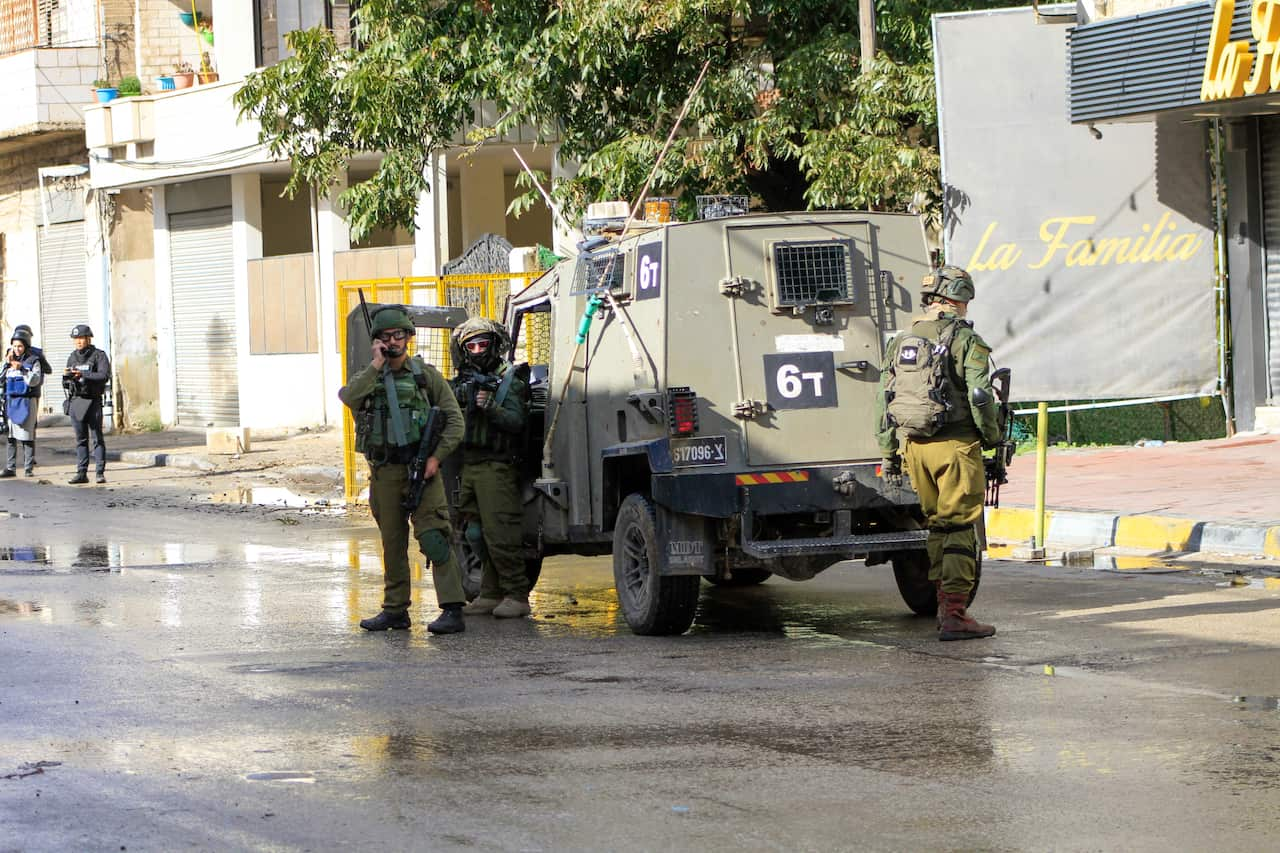 Image of military personnel in khaki uniform standing beside army vehicle.