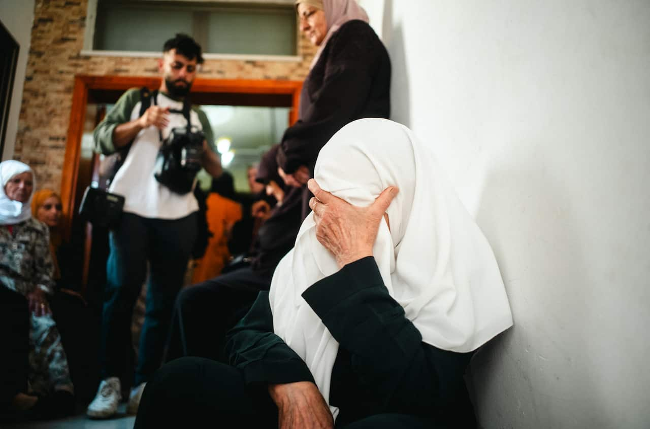 Image of a woman wearing a headscarf covering her face with her hand, others in background.