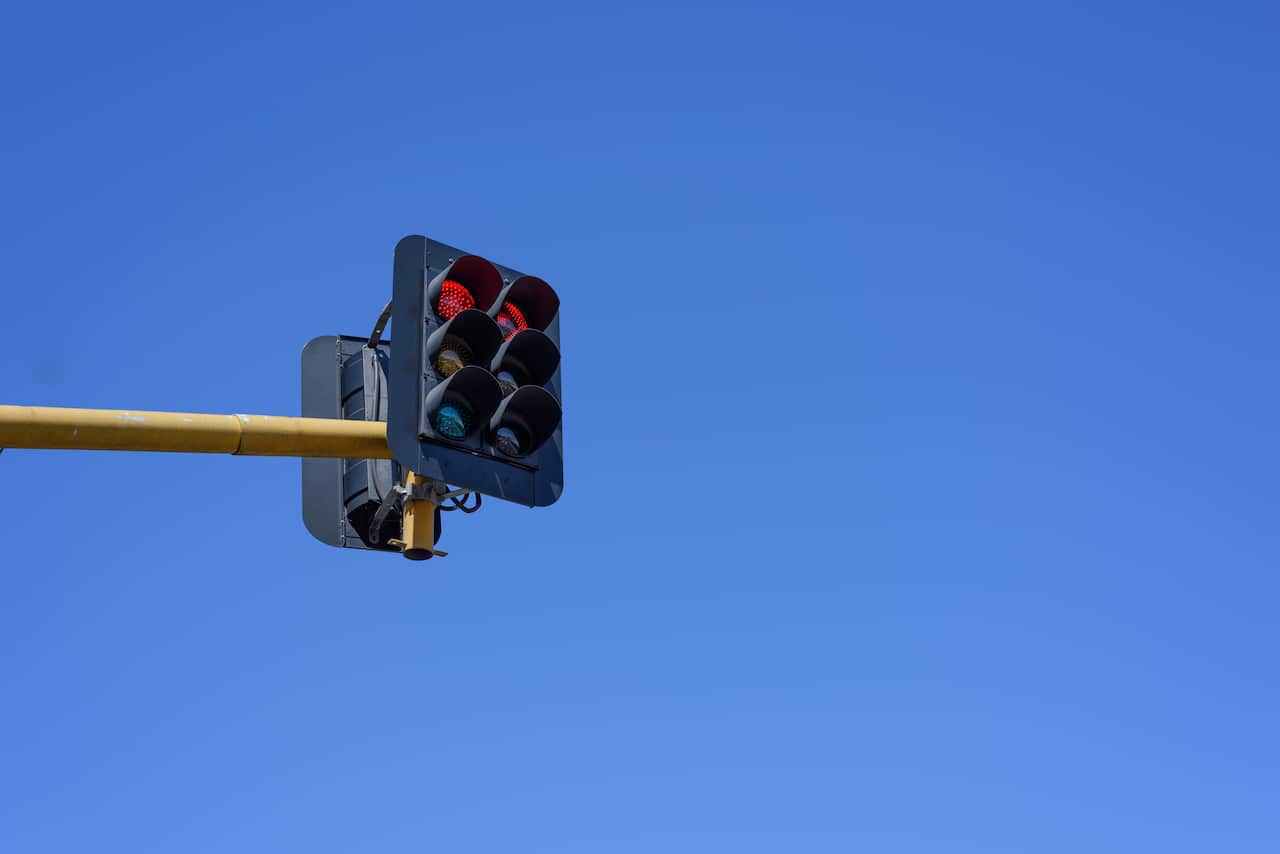 Image of red traffic light and turning arrow in a blue sky background.