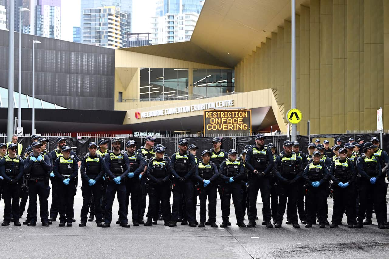 A line of police officers standing in front of a large building with "Melbourne Convention Exhibition Centre" written on it.