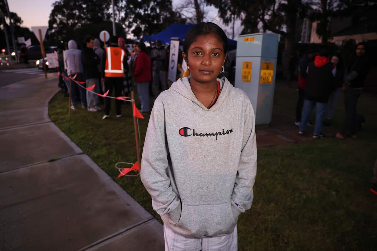 A teenage girl wearing a grey tracksuit poses in front of a sit-in protest