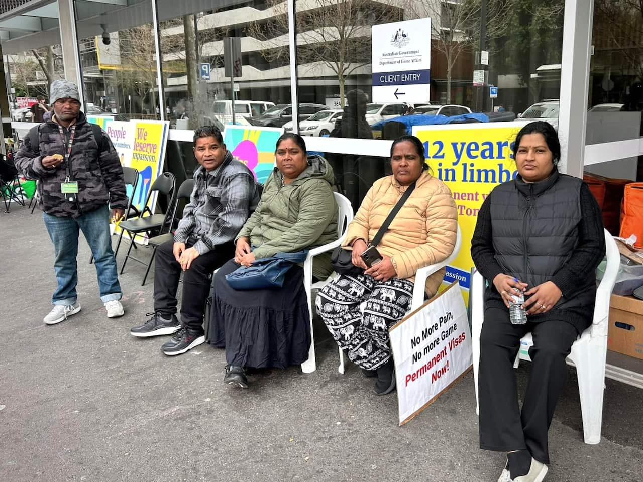 Five Tamil Sri-Lankan women sitting and standing outside a government office protesting for change.