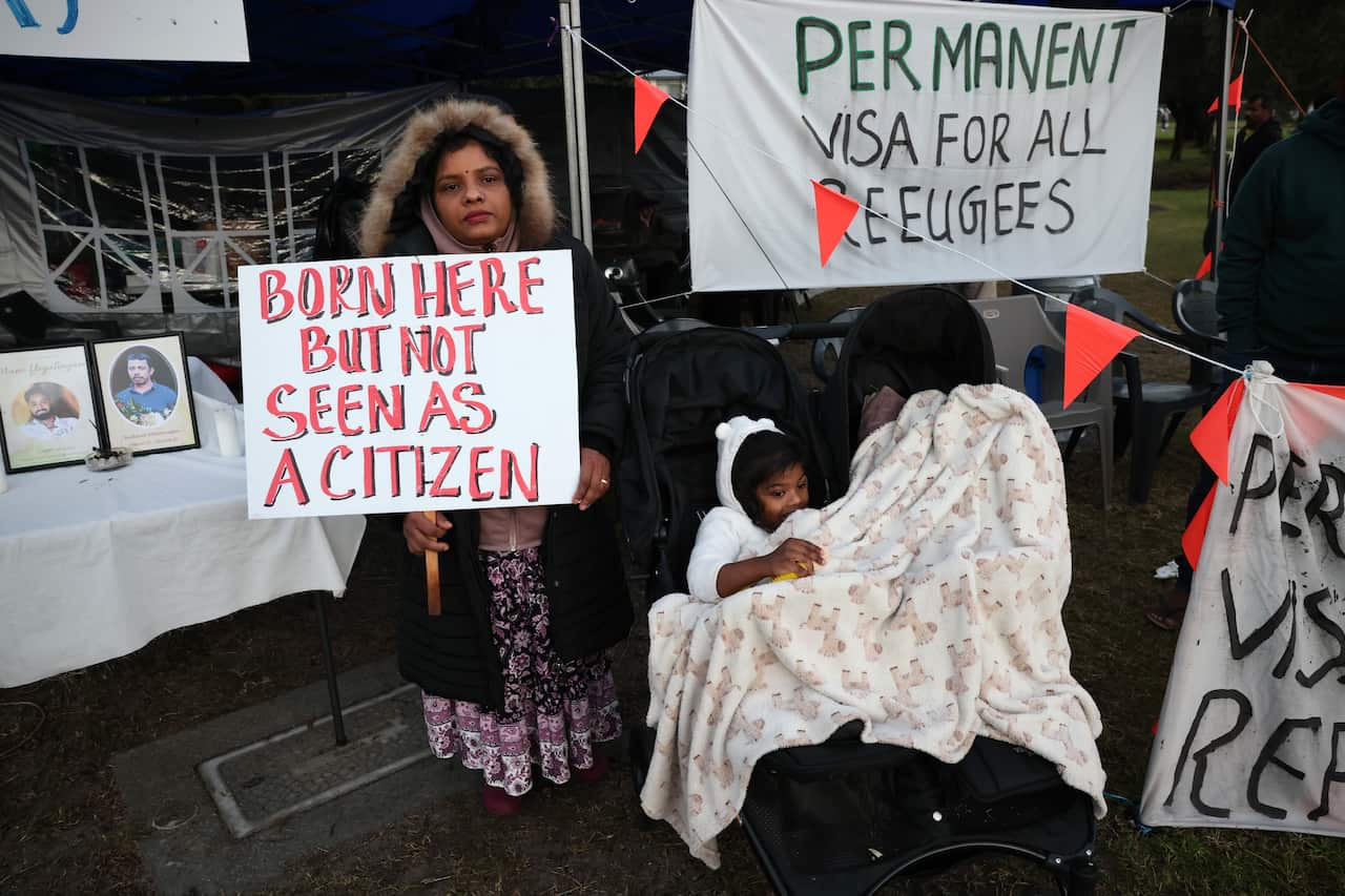 People outside an office. There are signs calling for permanent residency