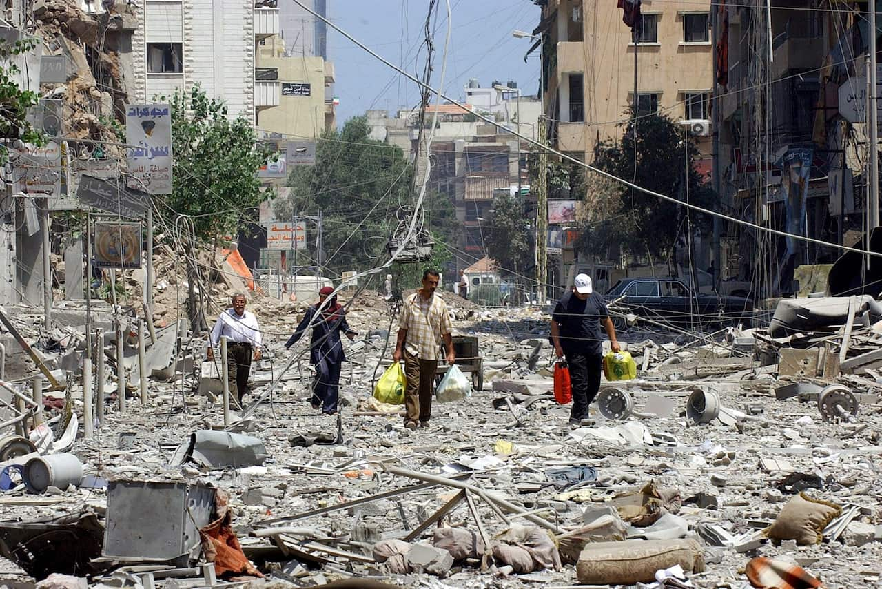 Men carrying colourful bags walk among the rubble.