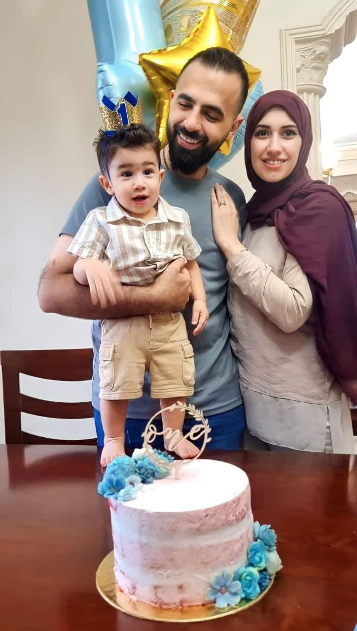 A couple holds a small child with a birthday cake sitting on the table.