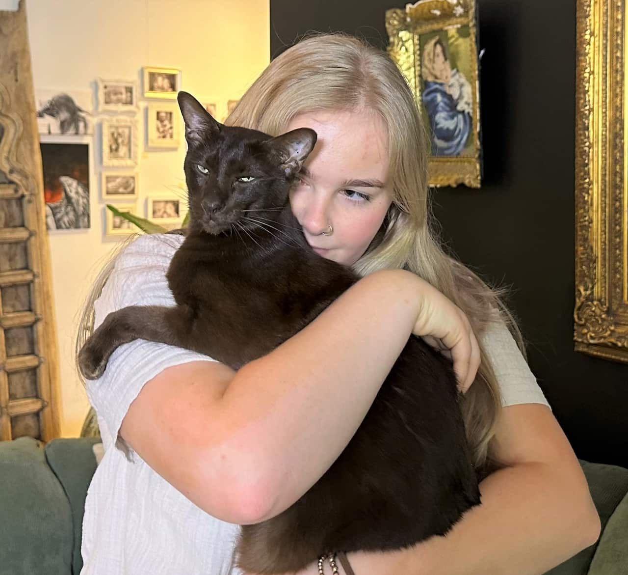 A woman with long hair hugs a black cat.