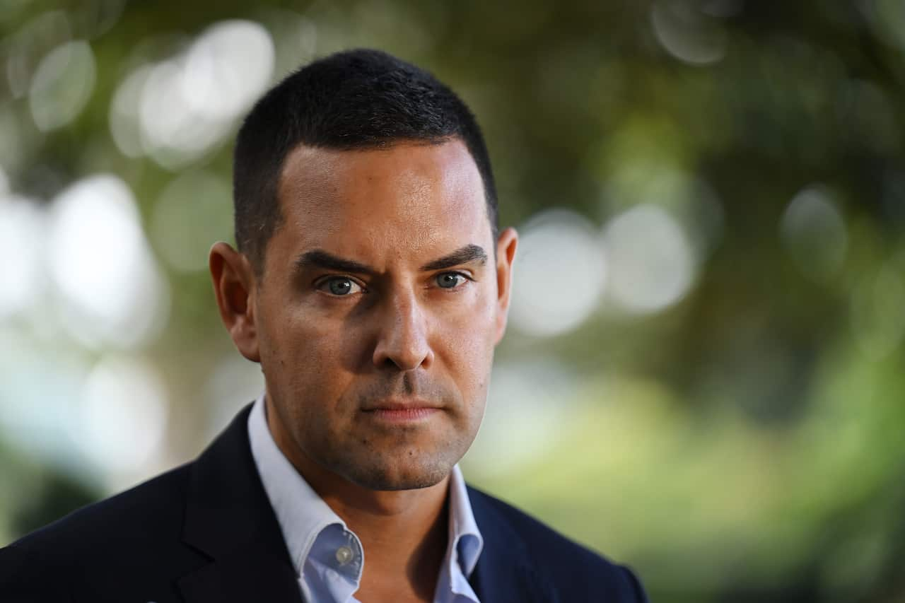 Alex Greenwich staring forward at a camera. There are blurred trees in the background behind him.