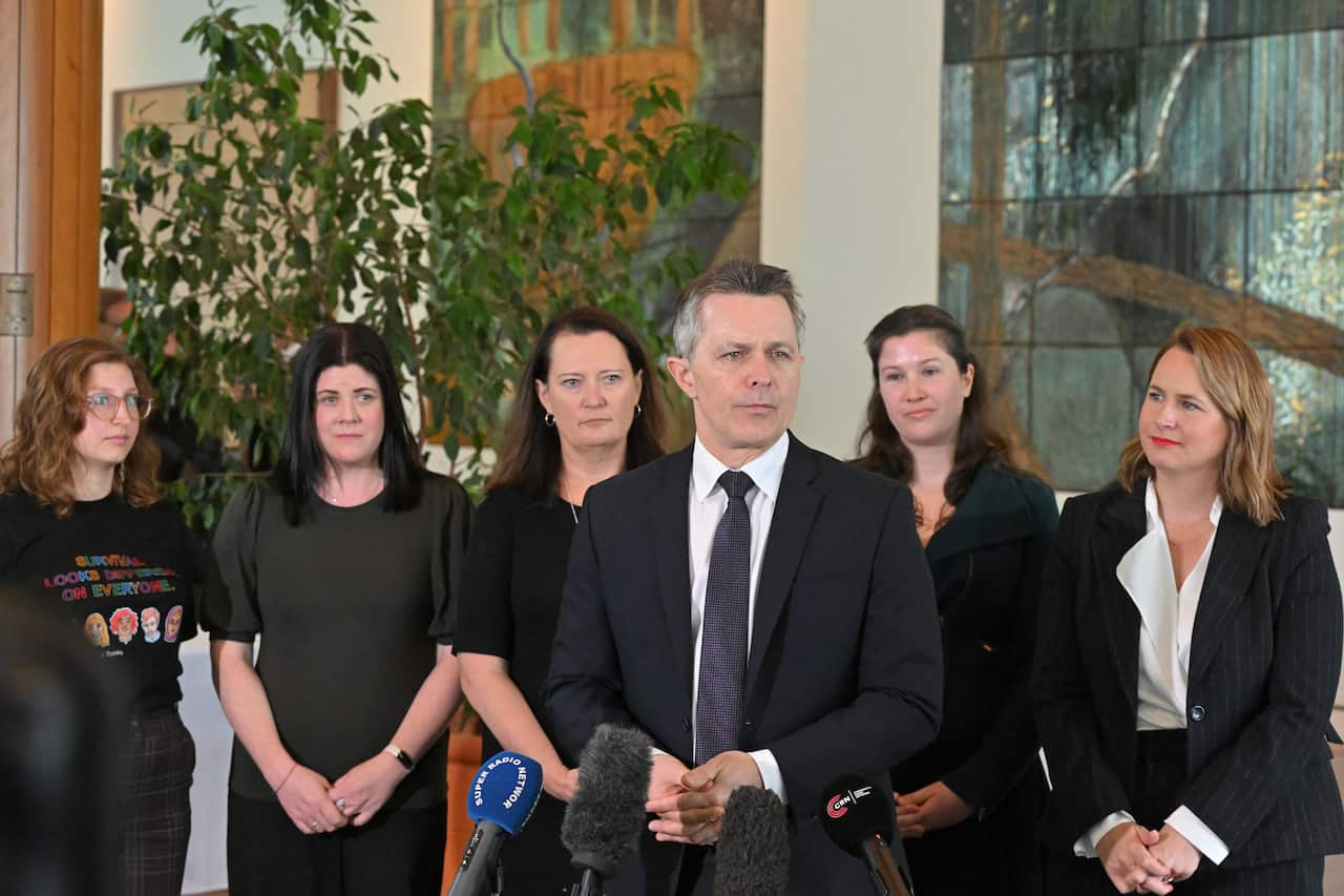 Five women stand behind a man in a suit.