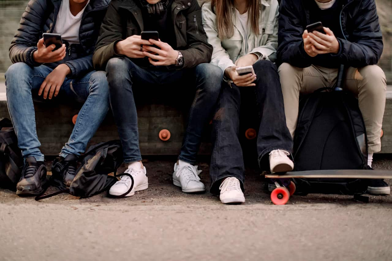 Four people sitting close together outside and looking at their phones