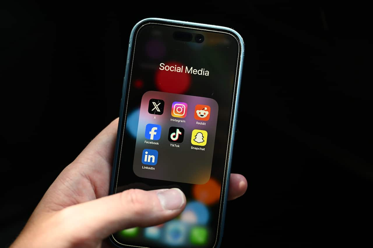 A hand holds an iPhone with social media icons on the screen.