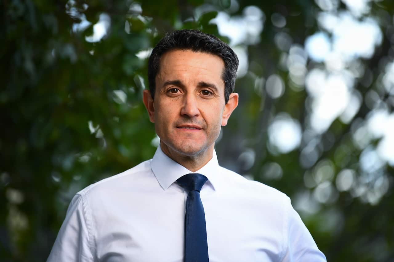 A man in a white shirt and blue tie standing in front of trees.