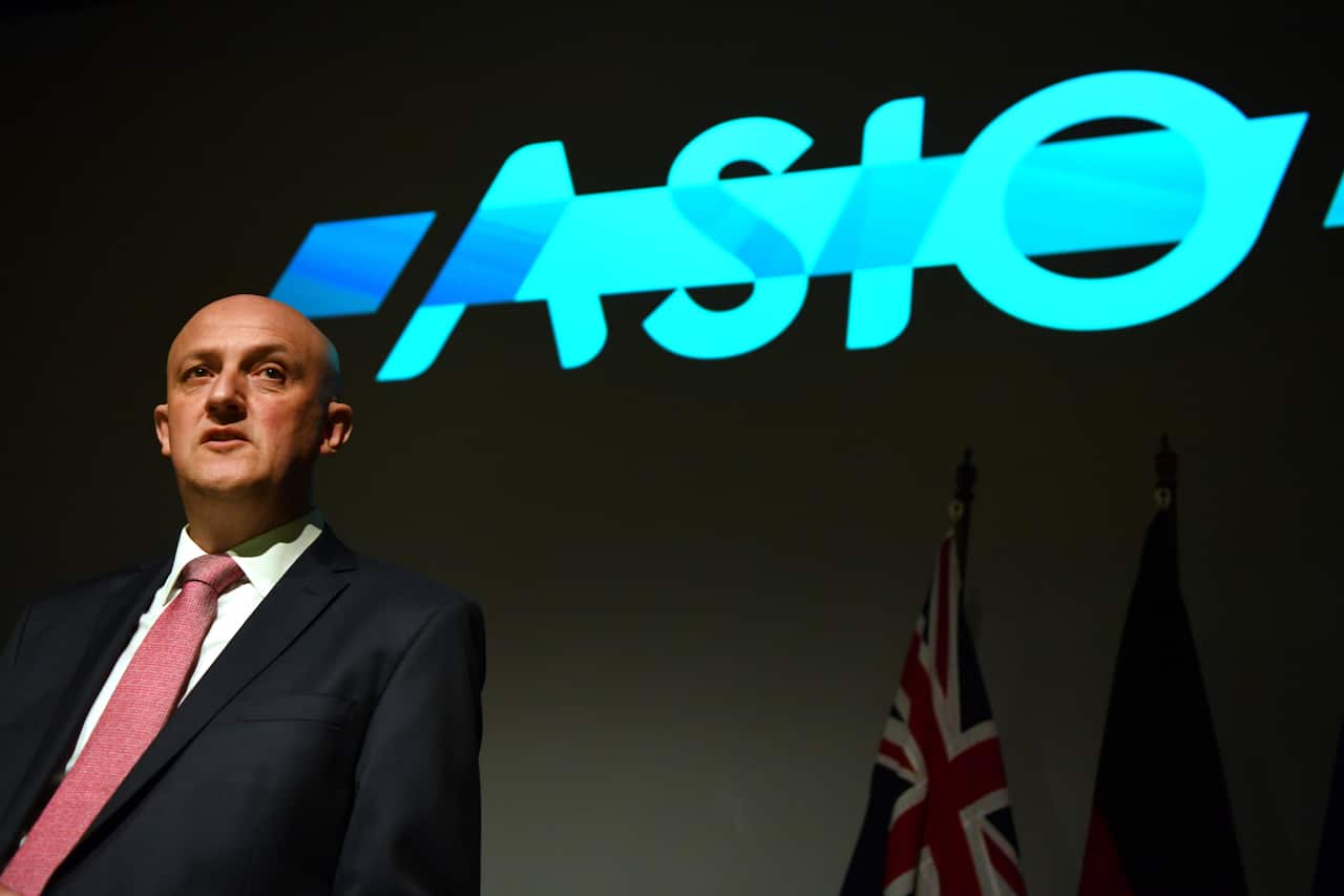 A man speaking while standing on a stage. A projection behind him reads "ASIO".