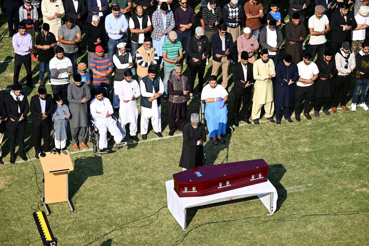 A crowd prays in front of a casket