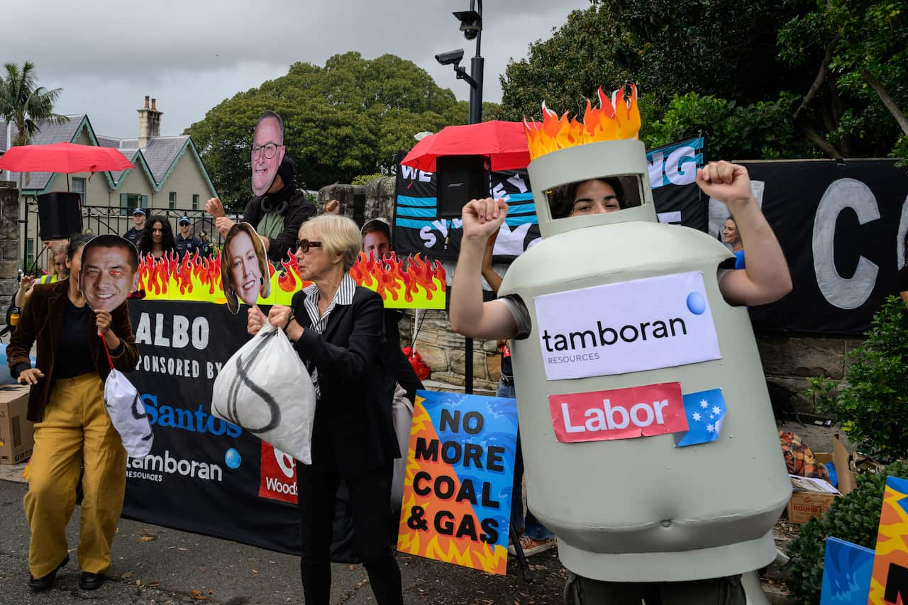 A protester wearing a costume of a fossil fuel tank, with "Tamboran Resources" and "Labor" signs on it. In the background other protesters hold prop money bags and placards demanding "No more coal and gas"