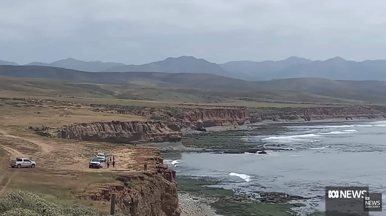 A wide shot of three vehicles parked near a cliff edge, with the ocean to the right.