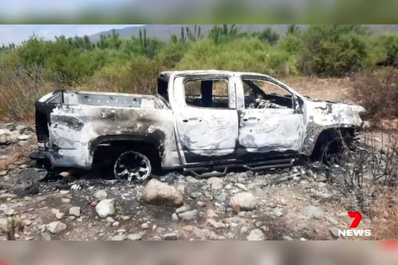 A burnt-out truck among rocks and grassland.