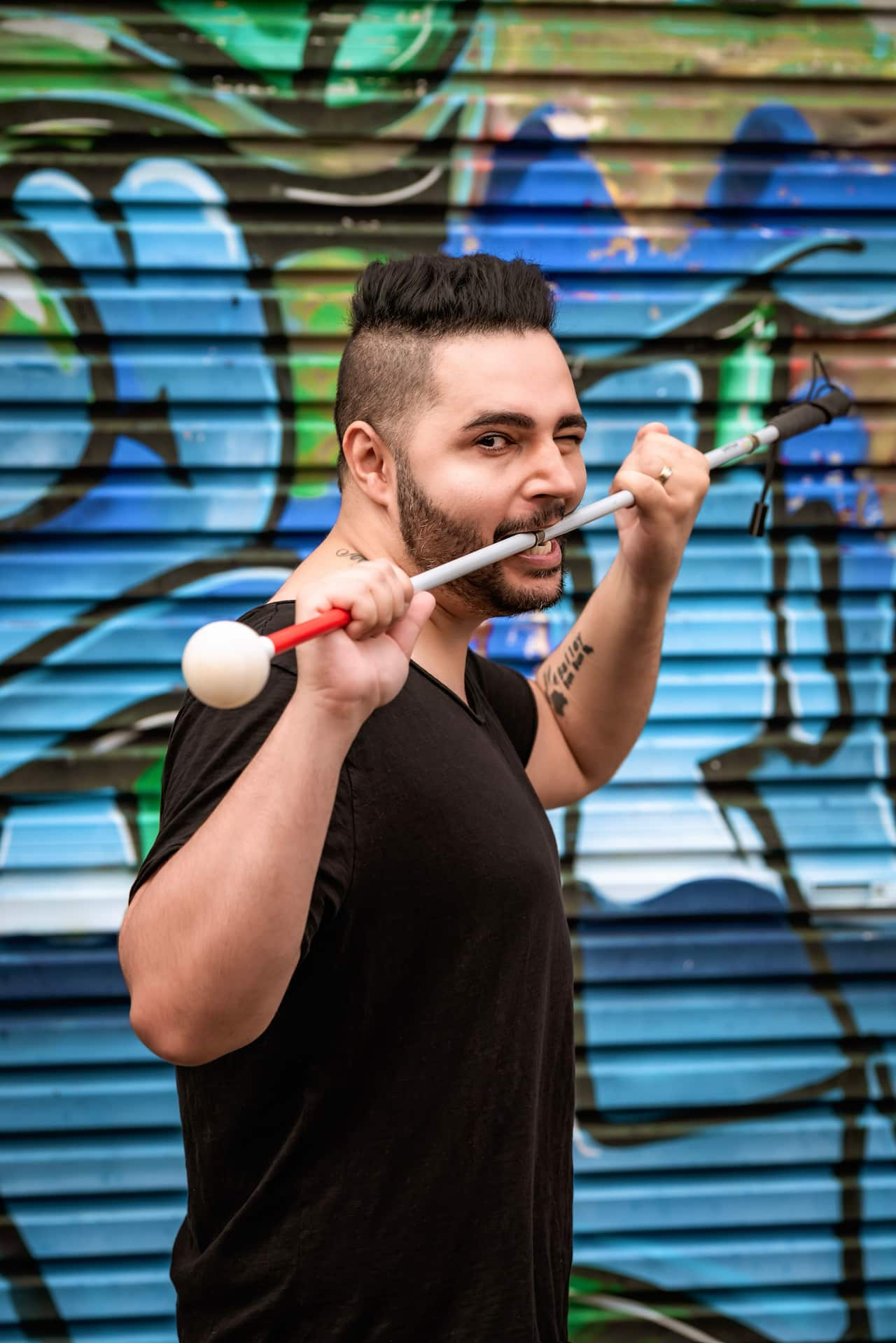 A man holding a white cane horizontally and biting into it 