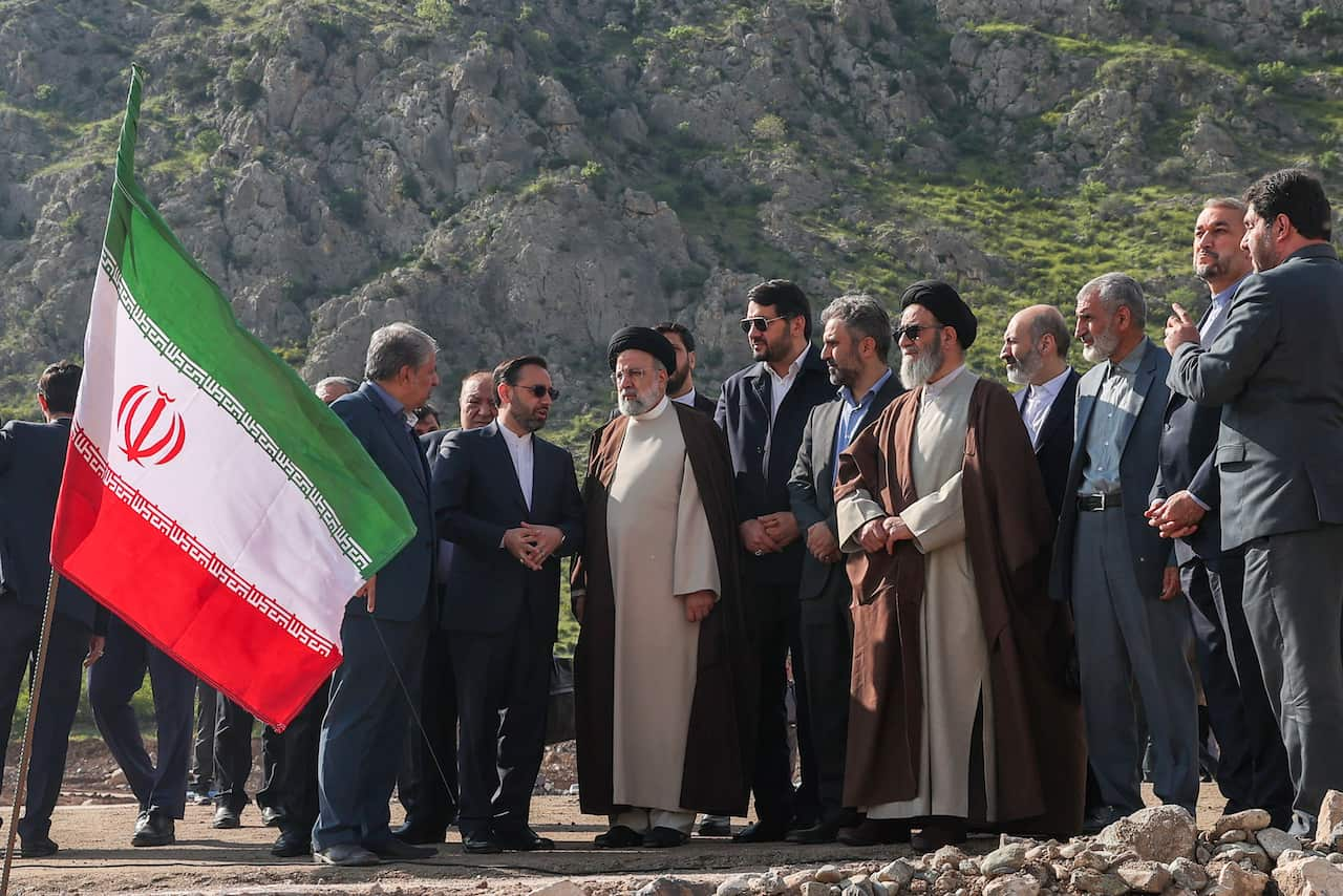 A group of men stand together near an Iranian flag.