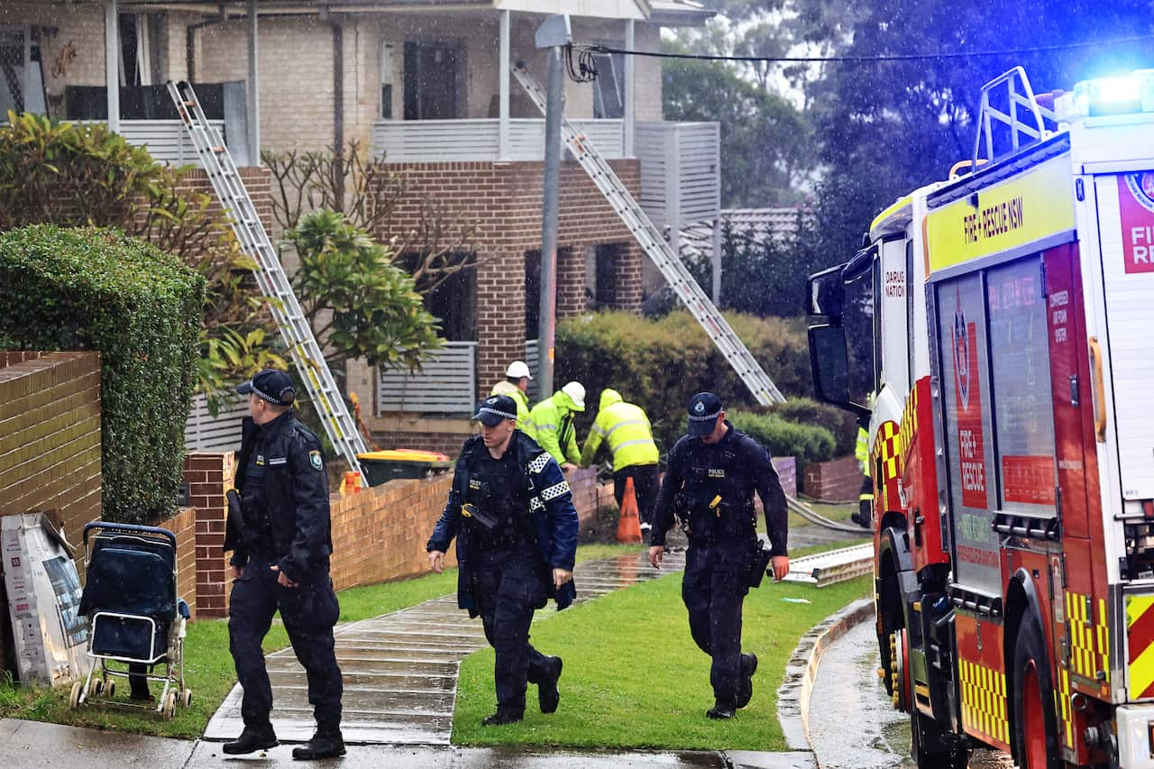 People in uniforms at a scene of a partial building collapse following an explosion.