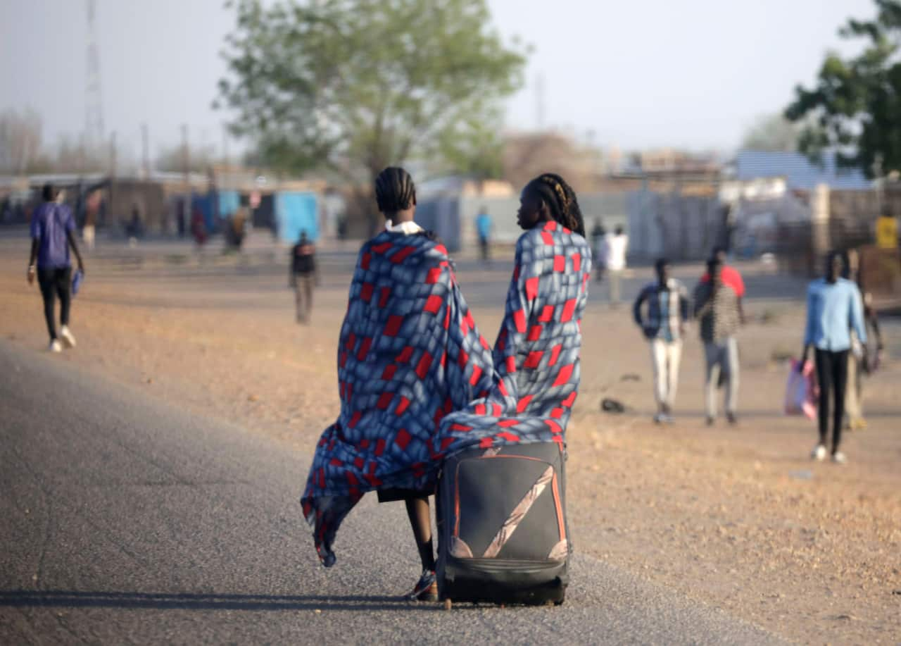 Two people pull a suitcase as they walk.