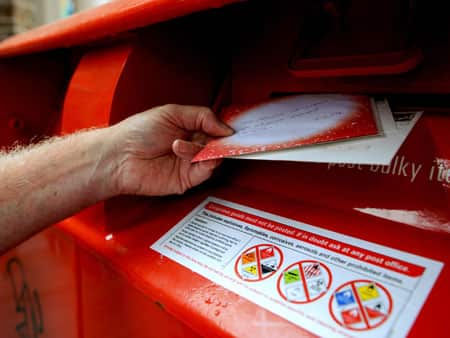 A hand places two letters into a red postbox