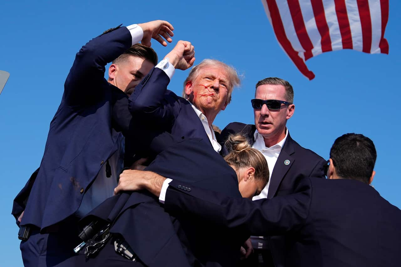 Donald Trump raises his fist in the air while held by secret service agents