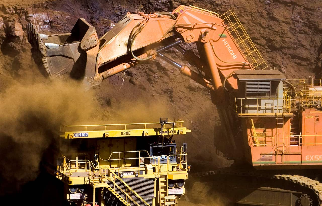 A large mining crane depositing dirt. A smaller yellow vehicle is next to it.