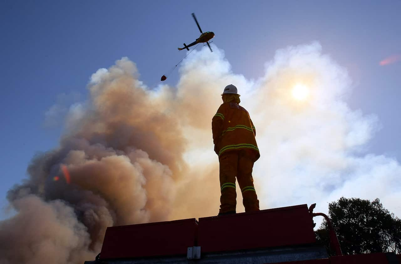 A firefighter standing watching a helicopter drop water on a firey cloud.