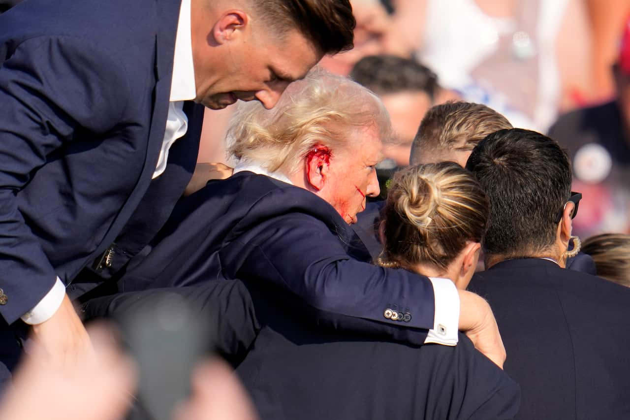 Donald Trump, his ear bleeding, gets carried away by three others