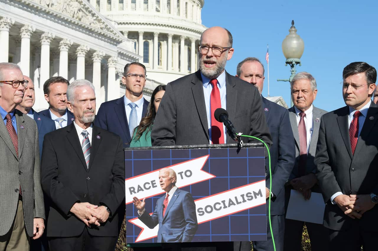 A man wearing a black suit and tie surrounded by men wearing suits speaks at a press conference