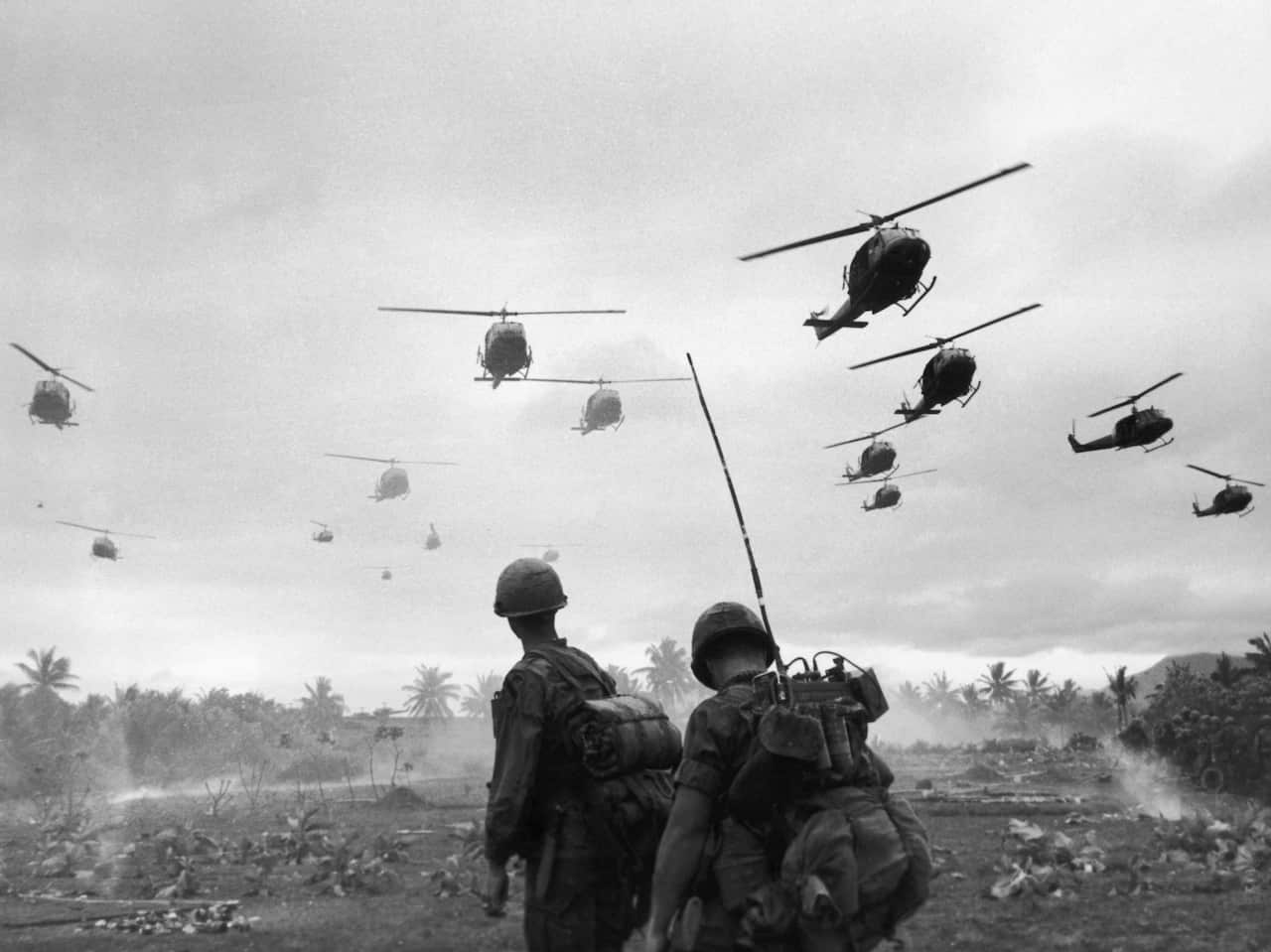 A black and white photo of two soldiers standing below helicopters