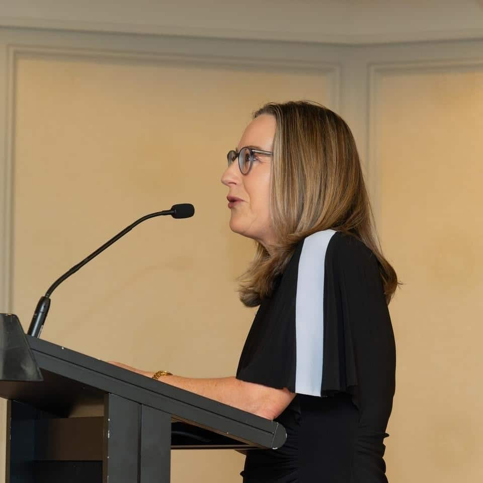 A woman speaking while standing at a lectern in front of a microhpone.