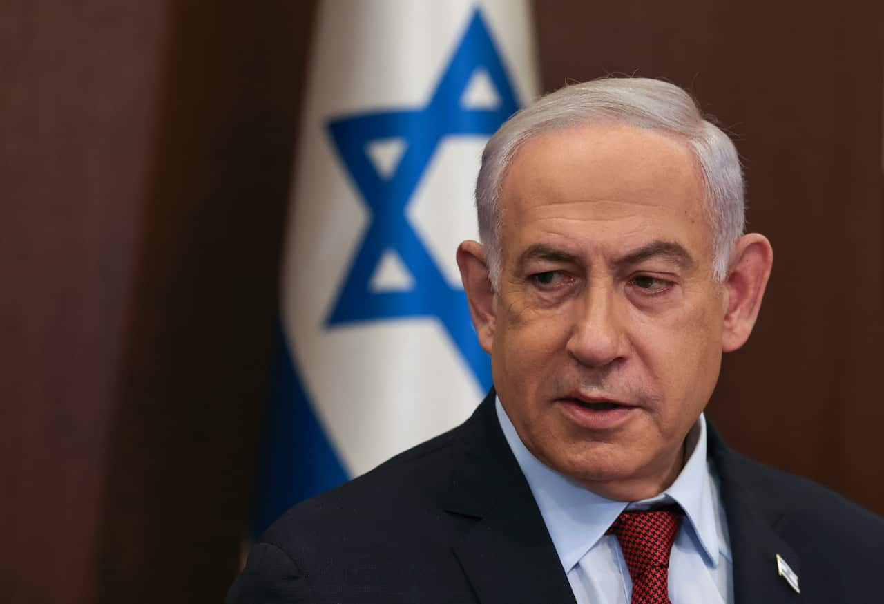 A man wearing a suit and tie standing in front of an Israeli flag.