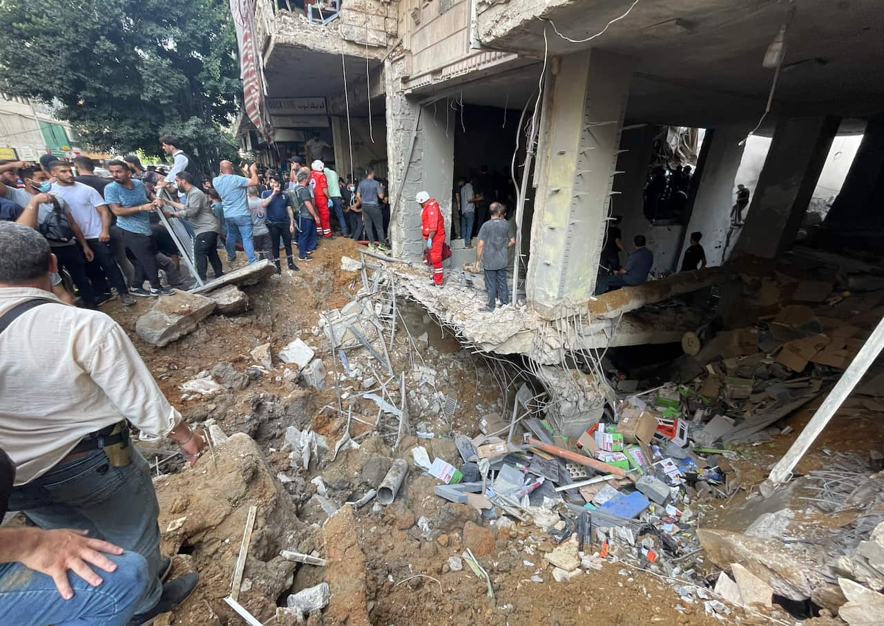 People stand amid the rubble of a building that has been severely damaged.