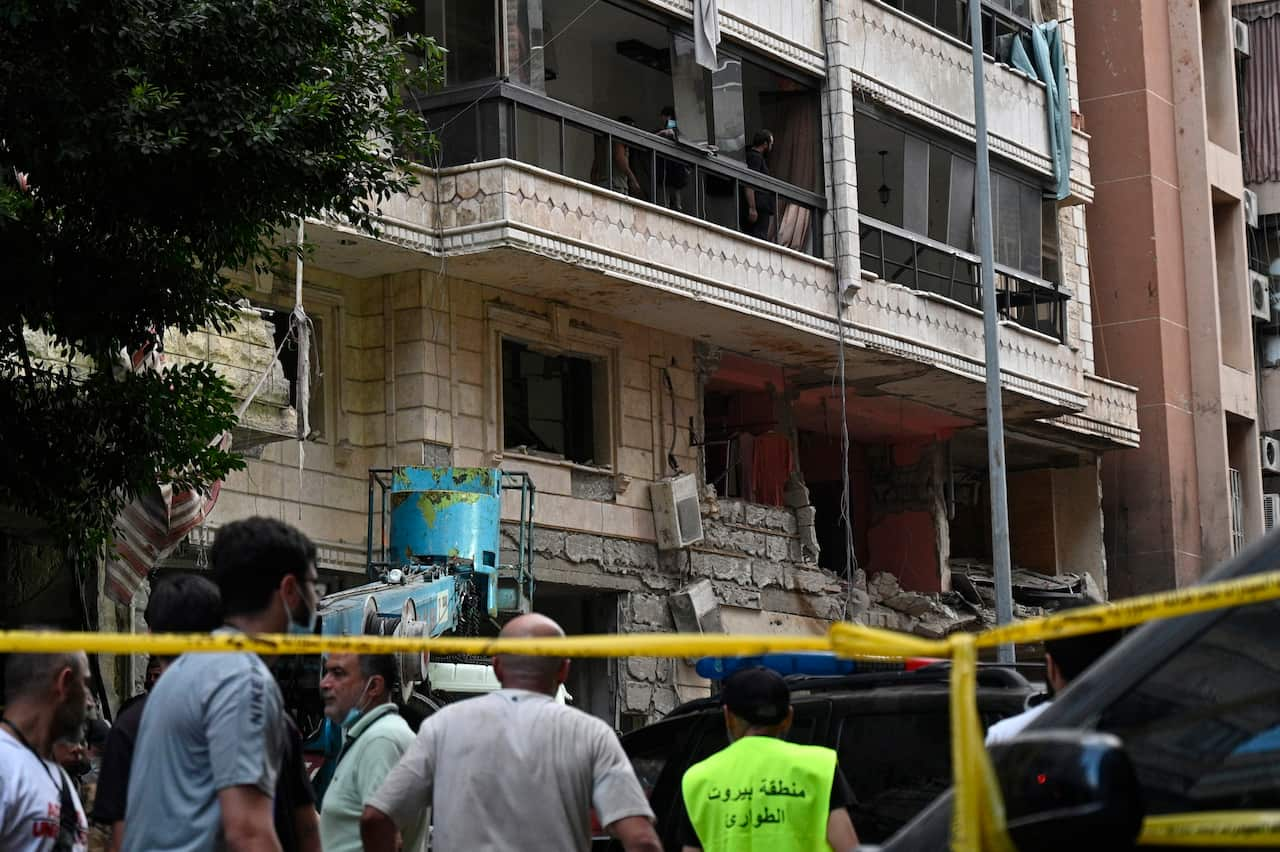 People stand outside a building that has been damaged. The area is taped off.